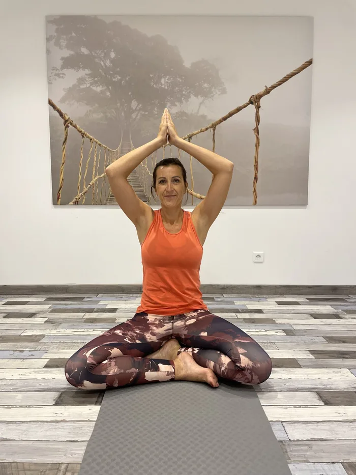 Laura en posture de méditation, bras levés au-dessus de la tête, dans la salle du studio